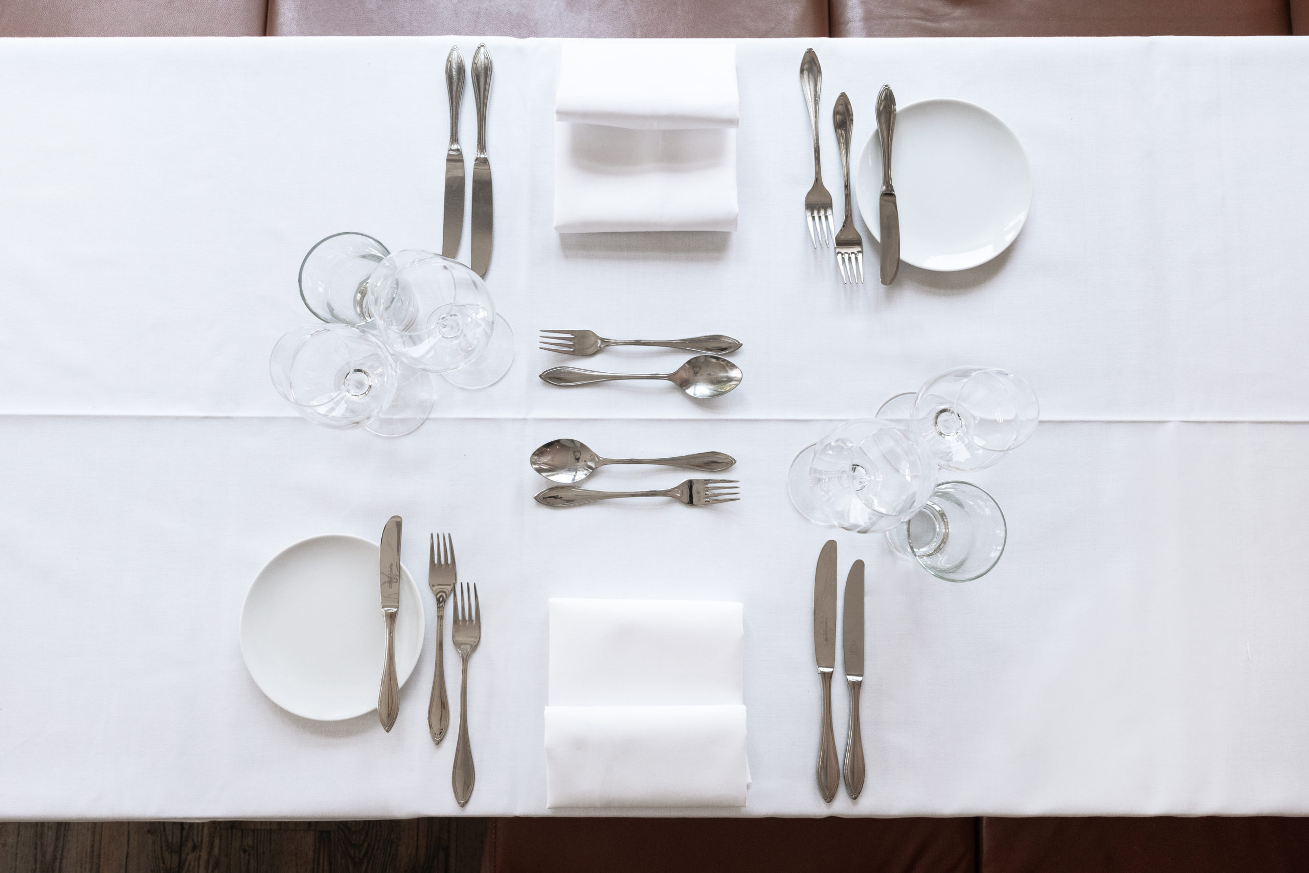 Ein vollständig edel gedeckter Tisch für zwei Personen mit drei Gläser, Brotteller und -Messer, Besteck für jeden Gang und mittig eine Serviette.